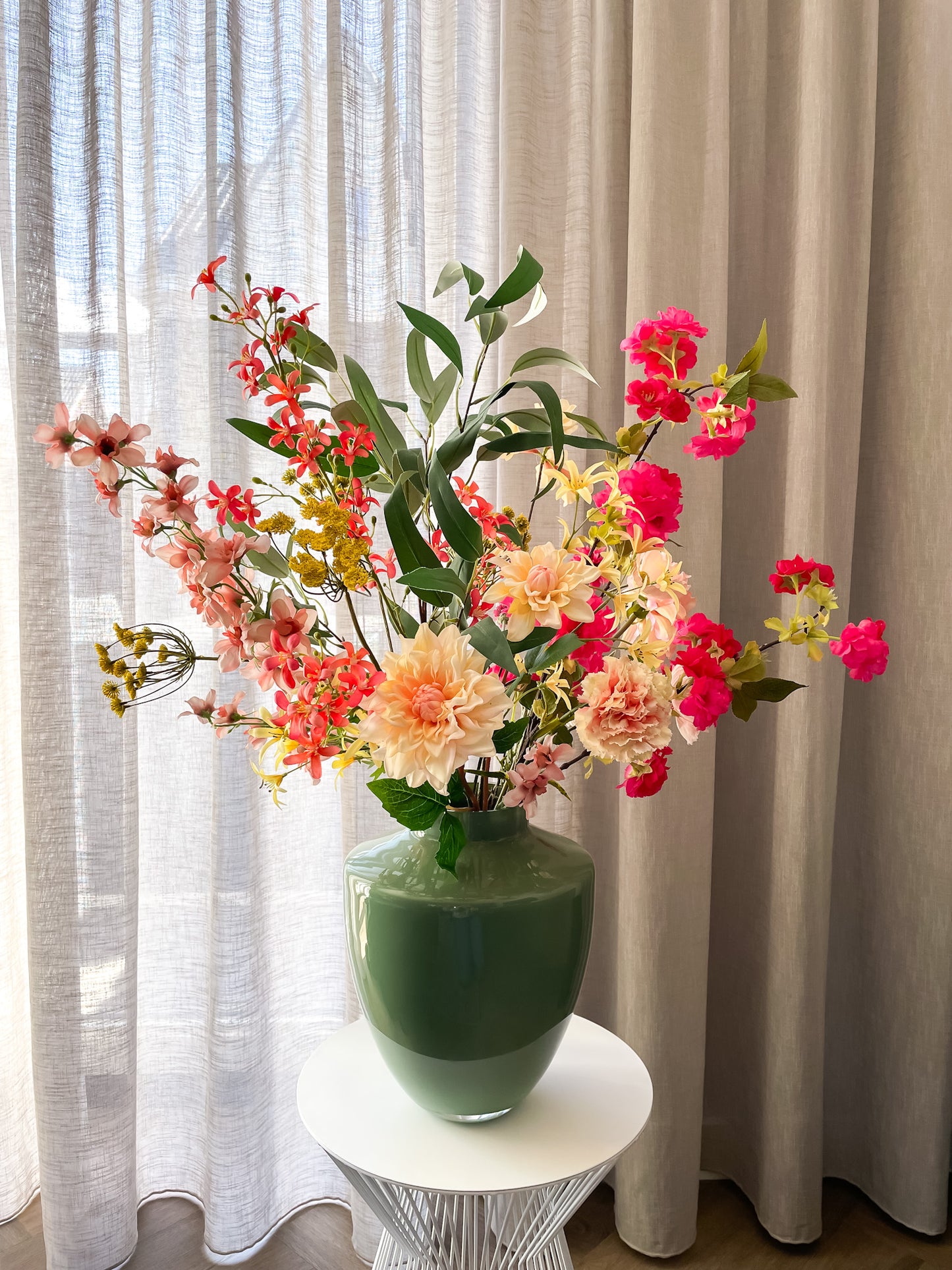 Vrolijk zijden boeket in roze, geel, oranje en perzik in een groene glanzende vaas