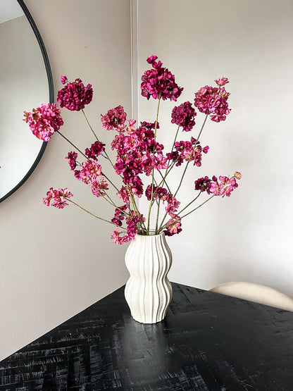Paarse en roze bloesemtakken in aardewerk vaas in creme