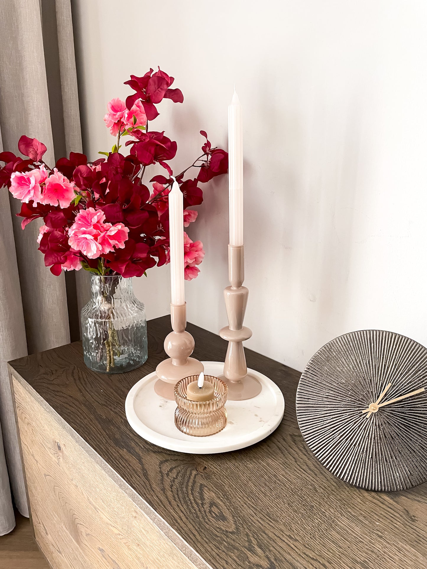 Unieke vorm kandelaren in beige kleur. Door de ronde vormen passen ze in ieder interieur. Gecombineerd met een zwarte tafelklok en roze zijden mini boeket.
