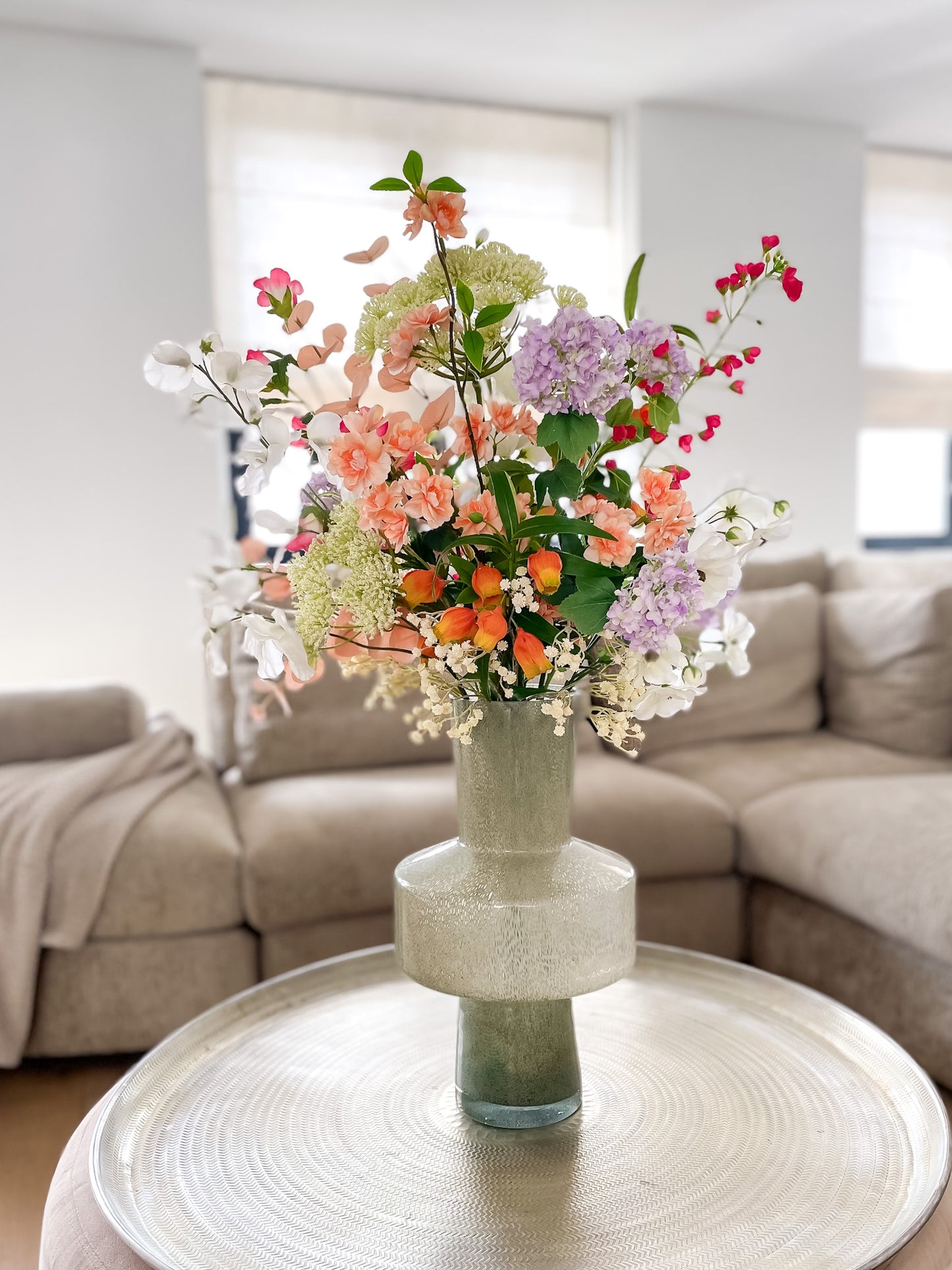 Zijden boeket in groene glazen vaas met bloemen in felroze, oranje, paars en groen