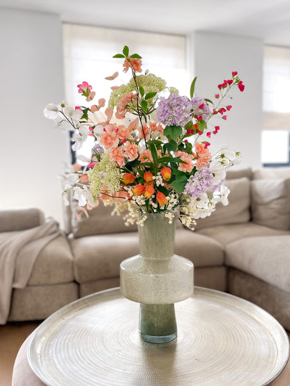 Zijden boeket in groene glazen vaas met bloemen in felroze, oranje, paars en groen