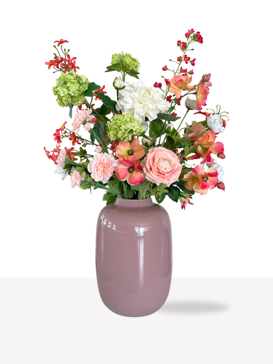 Zijden bloemen boeket met groene en oranje kleuren in pastel roze vaas. Geschikt als een luxe interieurdecoratie.