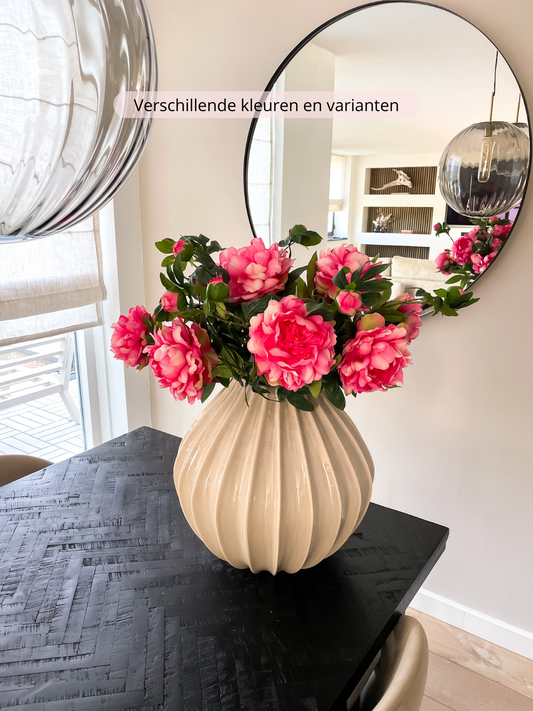 Zijden boeket met felroze pioenrozen in een geribbelde beige ronde vaas. Een luxe en vol boeket.