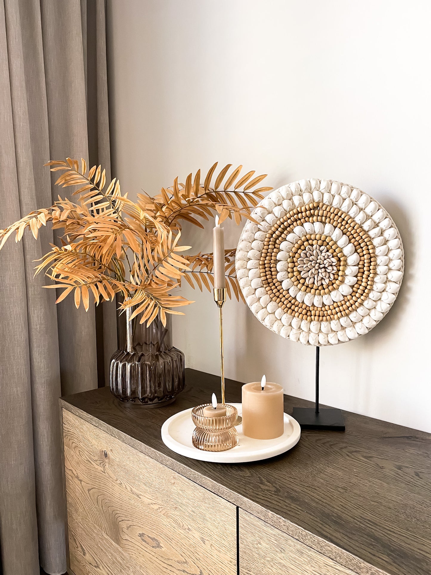 Groot schelpenornament in ronde vorm op zwarte standaard met witte schelpen en houten kralen. 