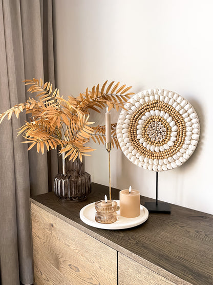 Groot schelpenornament in ronde vorm op zwarte standaard met witte schelpen en houten kralen. 