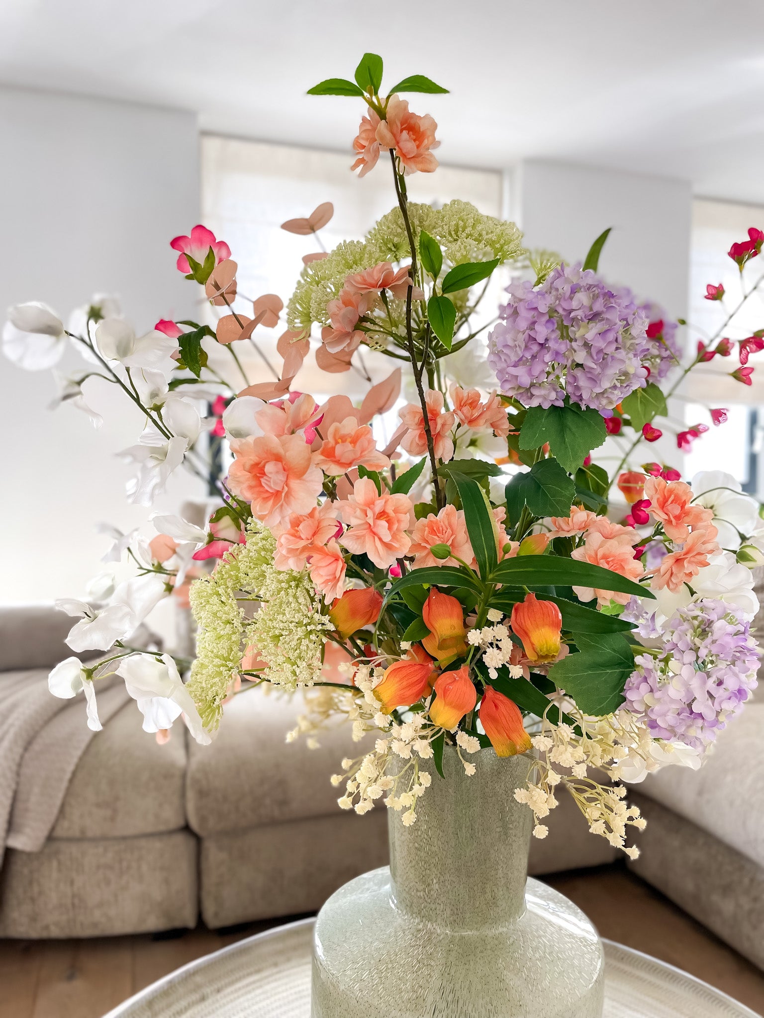 Kleurrijk zijden boeket met kunstbloemen in groene vaas, tinten felroze, oranje en paars.