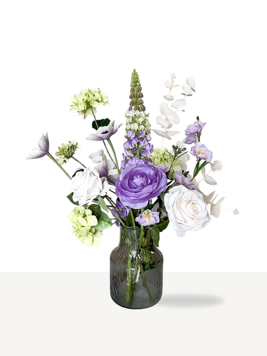 Een fris en vrolijk mini boeket met kunstbloemen zoals een roos, sneeuwbal hortensia, eucalyptusblad en ranonkel in zacht paarse, groene en witte kleuren.
