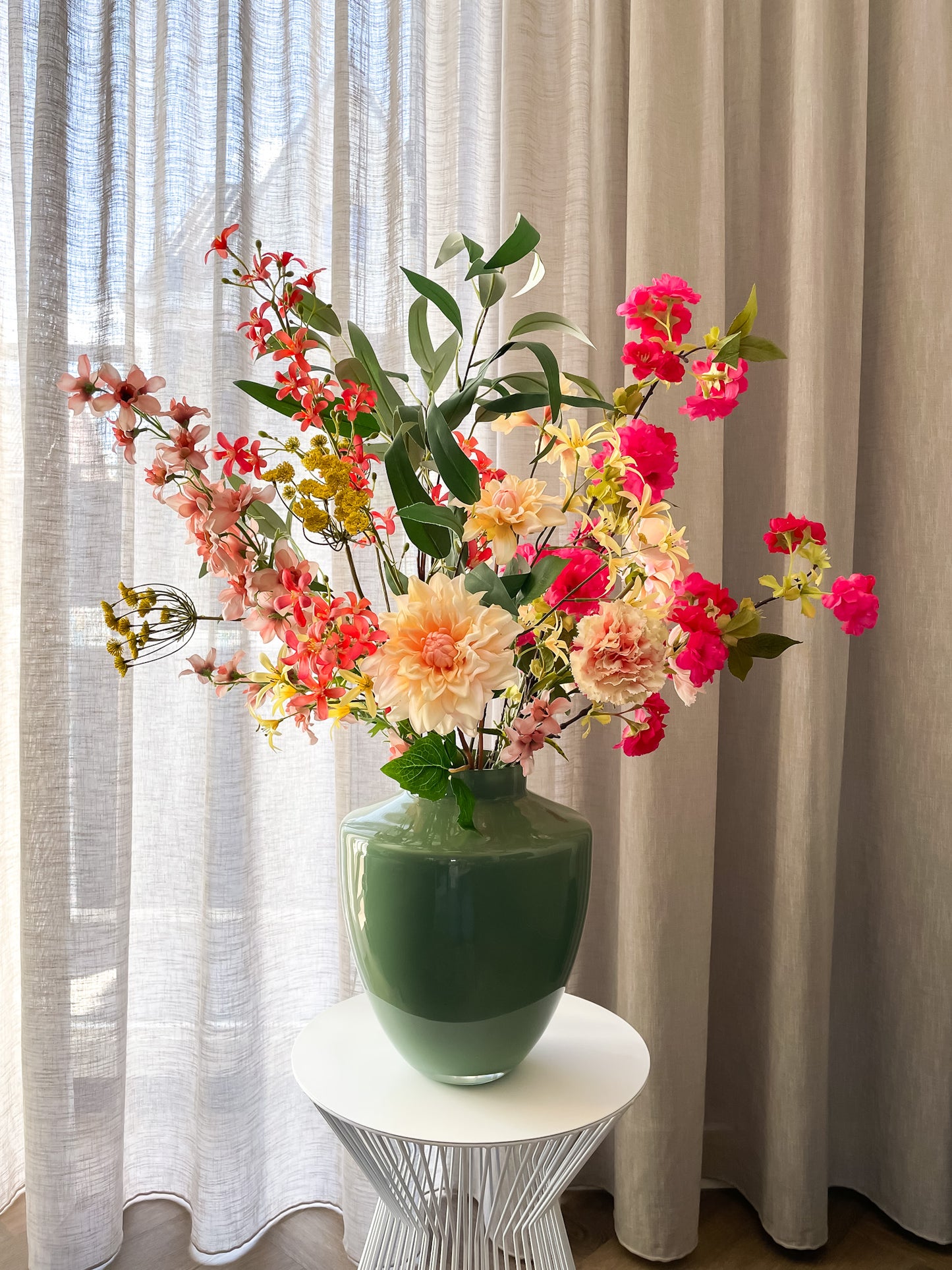 Elegant zijden boeket in roze, geel en perzik met groene bladeren in glanzende vaas