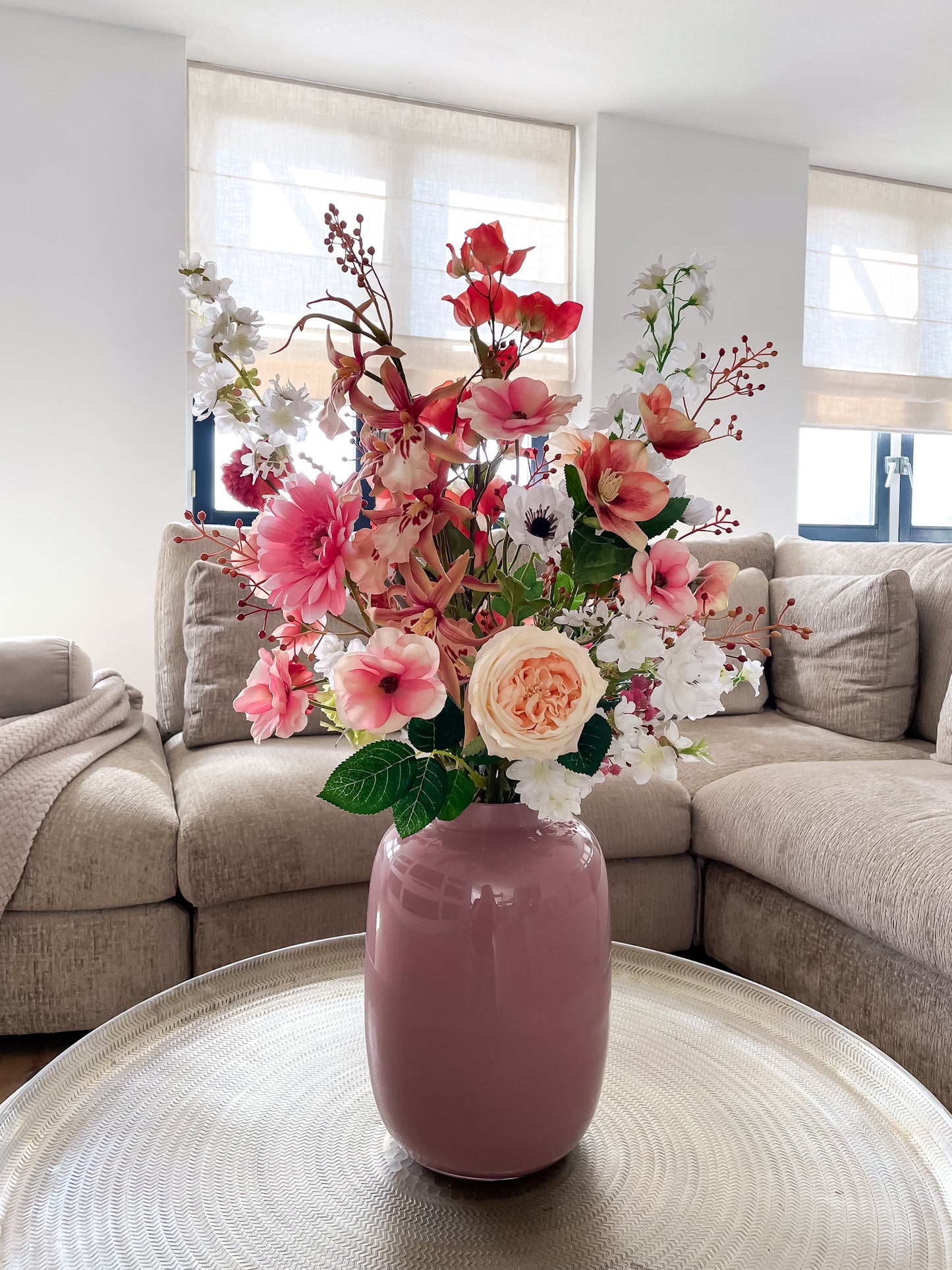 Vrolijk kunstbloemen boeket in roze, oranje en groen, gepresenteerd in roze glazen vaas.