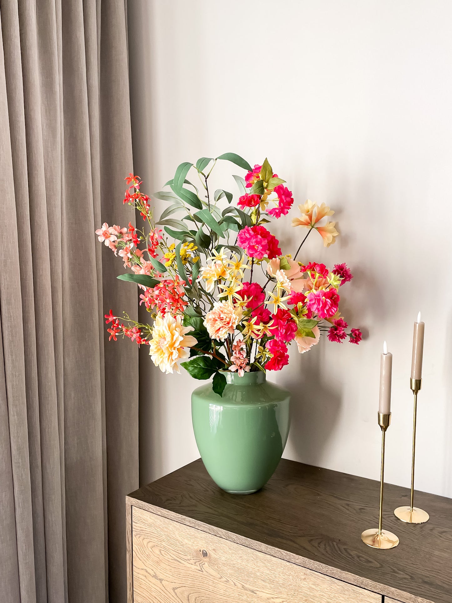 Zijden boeket met roze, gele, oranje, groene en perzikkleurige bloemen in een groene glanzende vaas