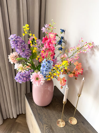 Mooie roze glazen vaas met kleurrijk zijden boeket in geel, roze, paars en blauw